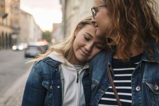 A teenage girl resting her head on her mother's shoulder