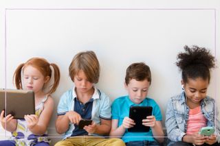 Four children sat against a wall watching a variety of screens