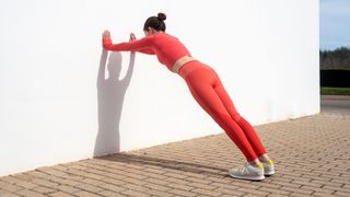 Woman doing wall push ups outdoors, wearing matching exercise clothes