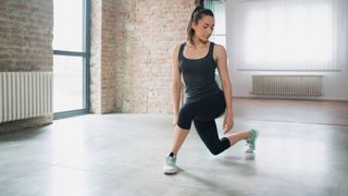 Woman doing curtsy lunge in a studio wearing workout clothes