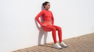 Woman doing bodyweight wall squat outdoors in the sunshine