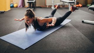 Woman doing superman exercise on yoga mat in the gym