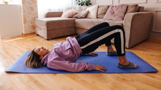 Woman doing glute bridge exercise on yoga mat in living room