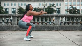 Woman doing sumo squats on path wearing workout clothes, arms out in front of her