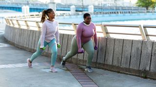 Woman doing walking lunge forwards along a riverside path