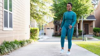 Woman standing upright in activewear on pathway outside house, wearing activewear