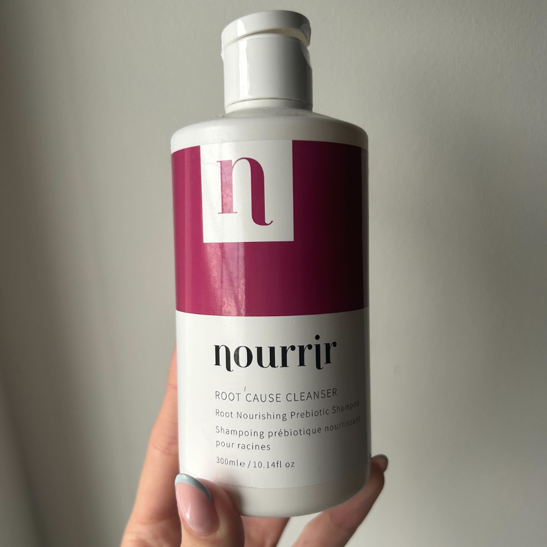 Hand holding Nourrir Root Cause Cleanse Shampoo with pastel blue French tip almond nails