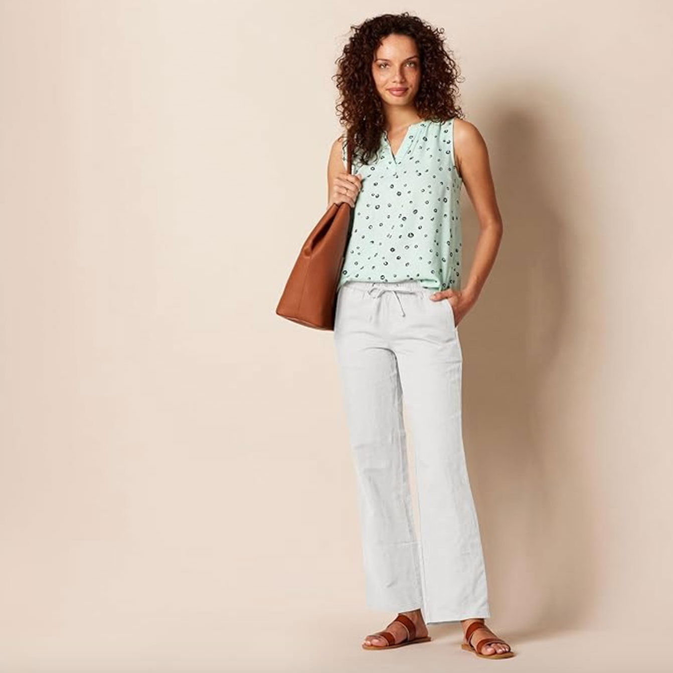 Woman wearing white linen pants, brown sandals, green top and brown bag