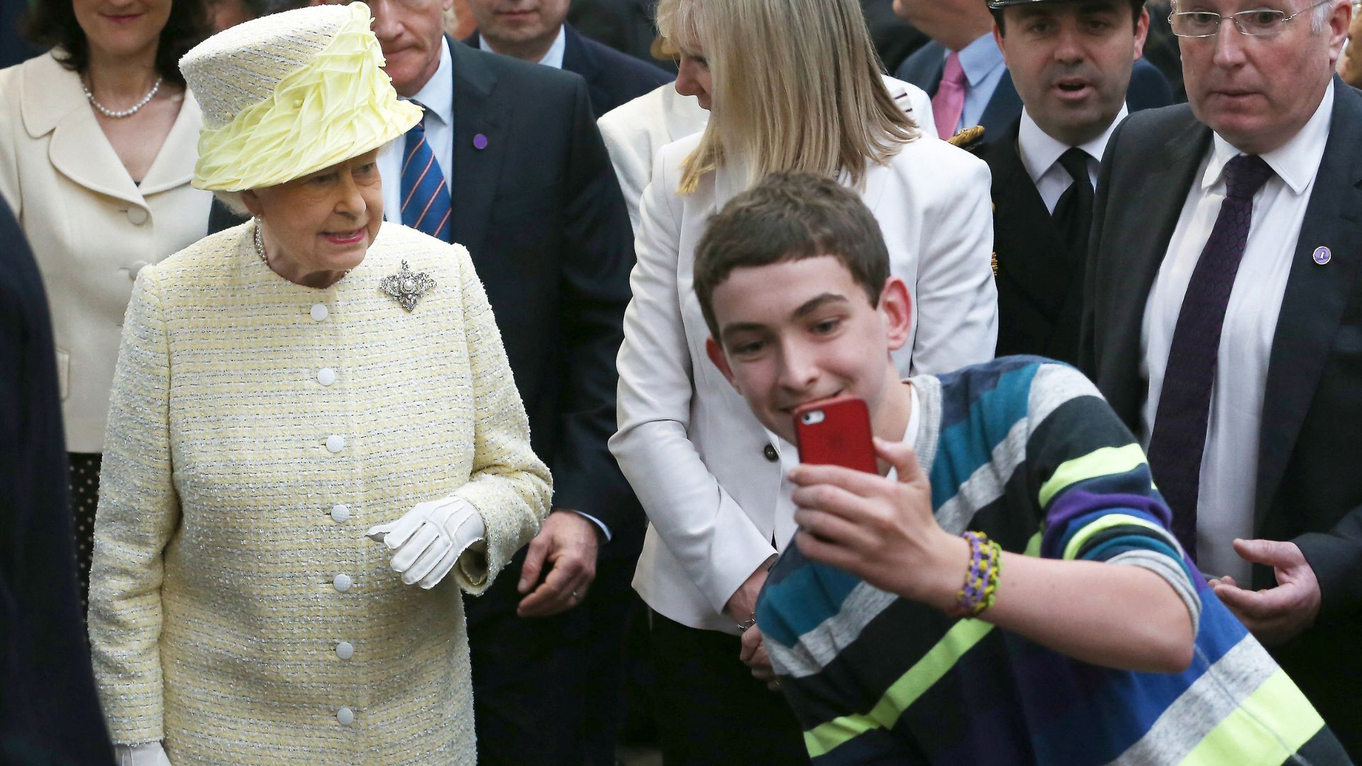 A young man takes a selfie with Queen Elizabeth II on his smartphone