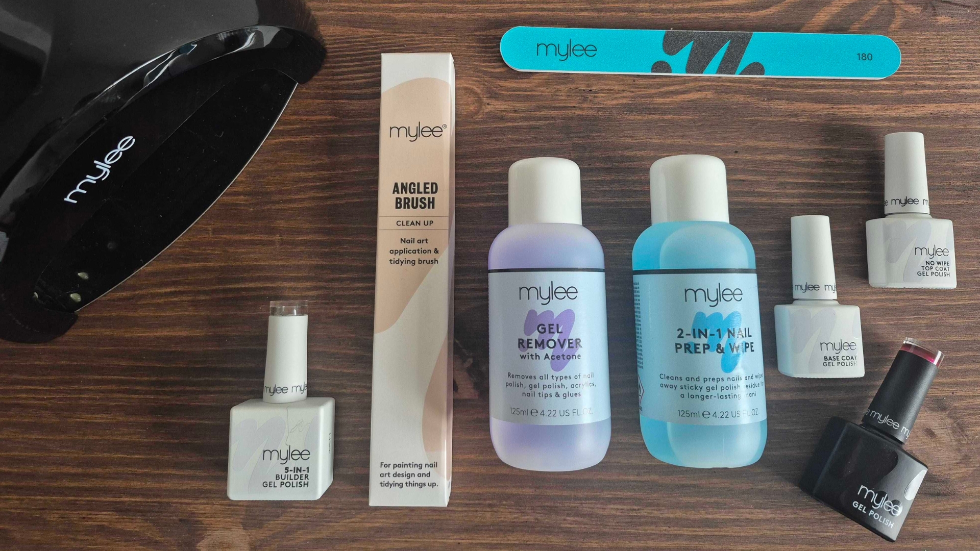A picture taken by Digital Beauty Writer, Naomi Jamieson, of her Mylee gel kit, featuring the brand's gel remover, 2-in-1 nail prep &amp;amp; wipe formula, a base and top coat gel polish, the burgundy gel polish in Diva, the Mylee curing lamp and a nail brush and file/ laid out on a wood background
